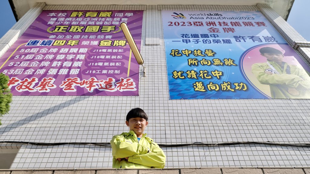 花壇國中外牆上貼著巨幅海報，2023「亞洲技能競賽」青少年組電氣裝配金牌許有崴得意的笑著。楊煥世攝